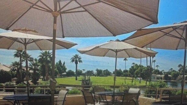 Uma área de pátio ao ar livre com vários guarda-sóis, cadeiras e vista para um campo de golfe.