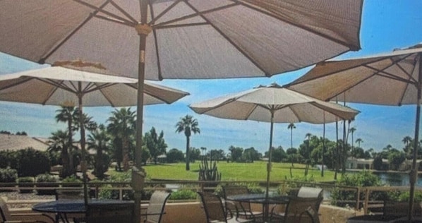 An outdoor patio area with multiple umbrellas, chairs, and a view of a golf course.