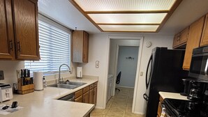 Uma cozinha compacta com armários de madeira, uma ilha central, frigorífico, fogão e micro-ondas.