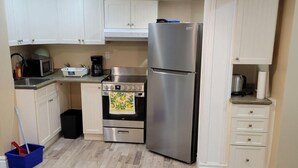 Une cuisine de taille réduite avec des meubles blancs, un réfrigérateur en acier inoxydable, un four à micro-ondes, une cuisinière et une machine à café.