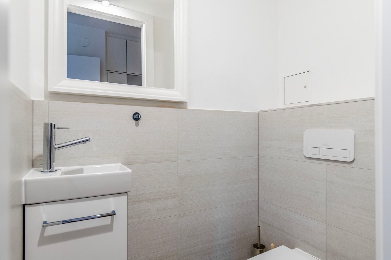 Een moderne badkamer met een witte wastafel, een spiegel erboven en een handdoekhouder.