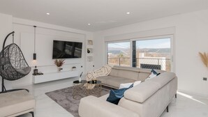 Un salon moderne avec un grand canapé, un fauteuil suspendu et un téléviseur à écran plat fixé au mur.