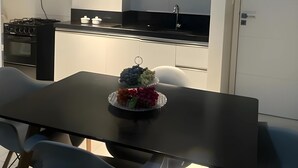 A modern kitchen with white cabinets, a black countertop, and a stainless steel stove. There is a bowl of fruit on the table. - Apto a 300m da Praia de Intermares  (Cabedelo)