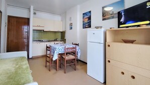 A compact kitchen with a dining table, chairs, a refrigerator, and a TV. - Enjoy the sun From our Lovely Terrace (San Michele al Tagliamento)