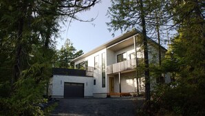 A modern two-story house with a garage, surrounded by dense forest.