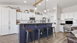 A modern kitchen with white cabinets, a dark island, bar stools, and pendant lighting.