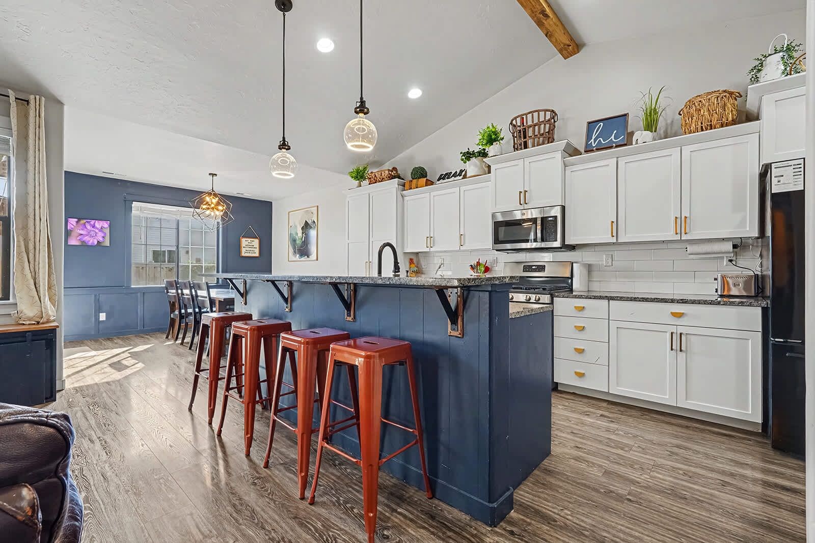 Une cuisine moderne avec des meubles blancs, un îlot central doté de tabourets et un coin repas avec un mur bleu et un plancher en bois.