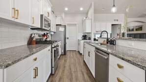 A modern kitchen with white cabinets, granite countertops, stainless steel appliances, and gold handles.
