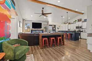 Una cocina moderna con techo de madera, una isla central con taburetes y un comedor con una silla verde.