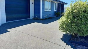A modern single-story house with a dark blue exterior, a garage door, and a small front yard with a bush.