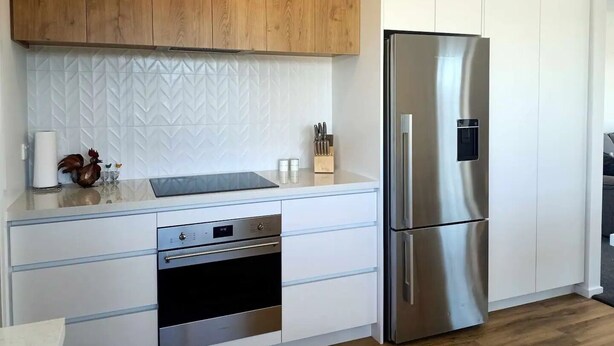 A modern kitchen with wooden cabinets, a stainless steel refrigerator, and a built-in oven.
