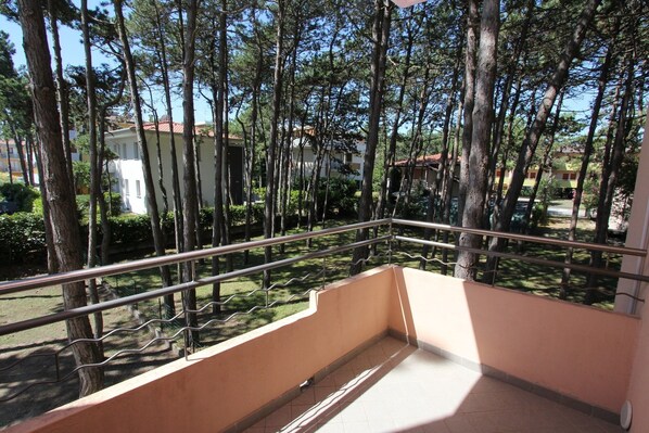 A balcony with a metal railing, overlooking a garden with trees and buildings in the background. - A Calm Escape Close to the Beach - Beahost (San Michele al Tagliamento)