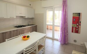A kitchen with white cabinets, a gas stove, and a dining table with a fruit bowl. - A Calm Escape Close to the Beach - Beahost (San Michele al Tagliamento)