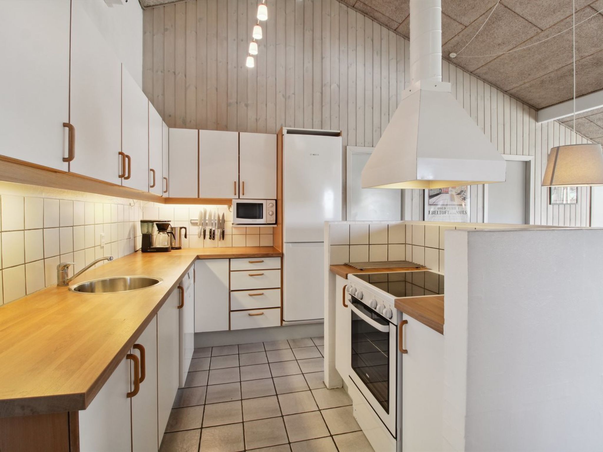 Una cocina moderna con armarios blancos, encimera de madera, microondas, cocina y una lámpara colgante.
