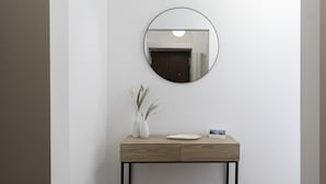 Een minimalistische console tafel met een ronde spiegel, een witte vaas met gedroogde planten, en een bordje met de tekst 