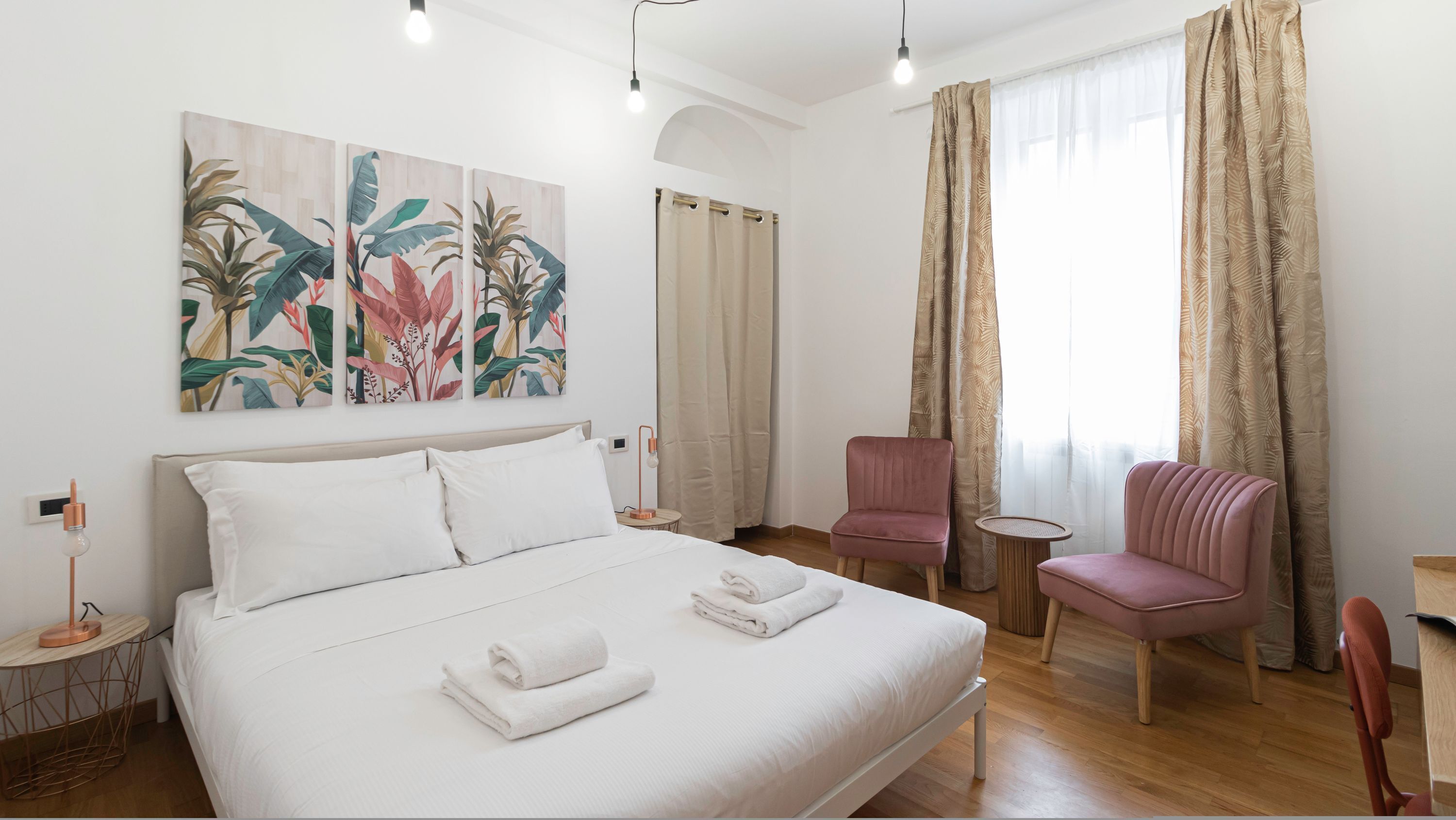 A hotel room with a bed, two chairs, a small table, and a painting on the wall.