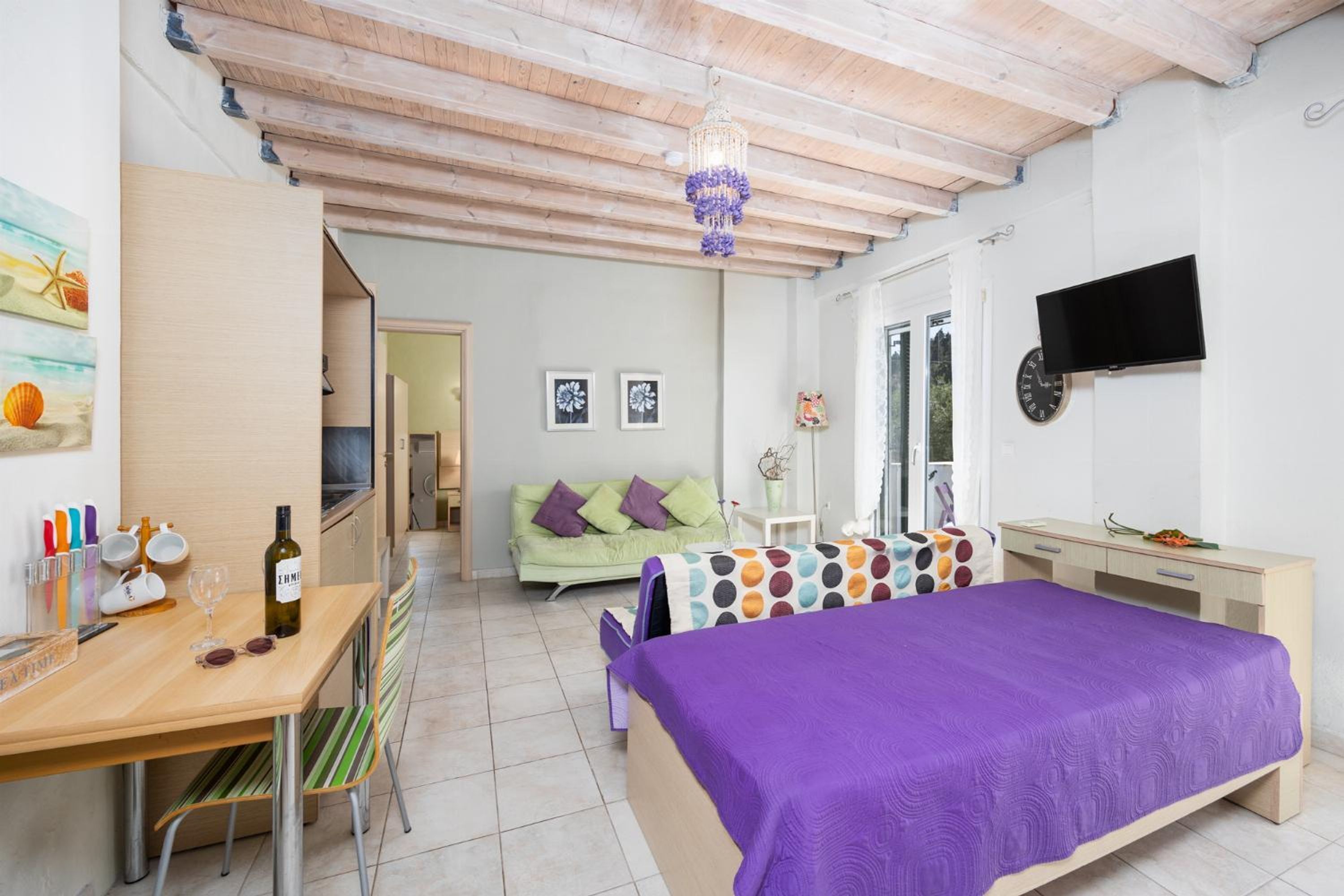 A bedroom with a bed, a desk, a TV, and a window.
