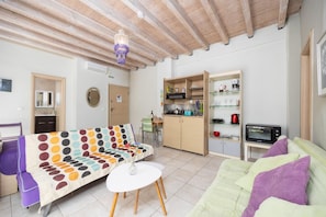 Un espacio habitable compacto con sofá, una mesa de comedor, kitchenette y techo con vigas a la vista.