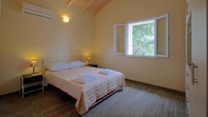 A bedroom with a bed, bedside lamps, a window, and an air conditioning unit.