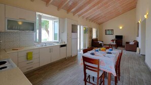 A spacious kitchen with wooden beams, a dining area with a table set for four, and a living area with a sofa and TV.