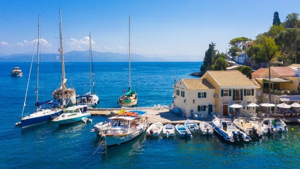 A marina with various boats docked, a building with a tiled roof, and a clear blue sky.