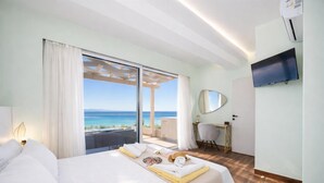 A hotel room with a bed, a desk, a chair, a TV, and a view of the ocean. - Villa Alora in Mparmpati (Corfu)