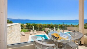 A balcony with a view of the sea, a pool, and outdoor furniture. - Villa Alora in Mparmpati (Corfu)