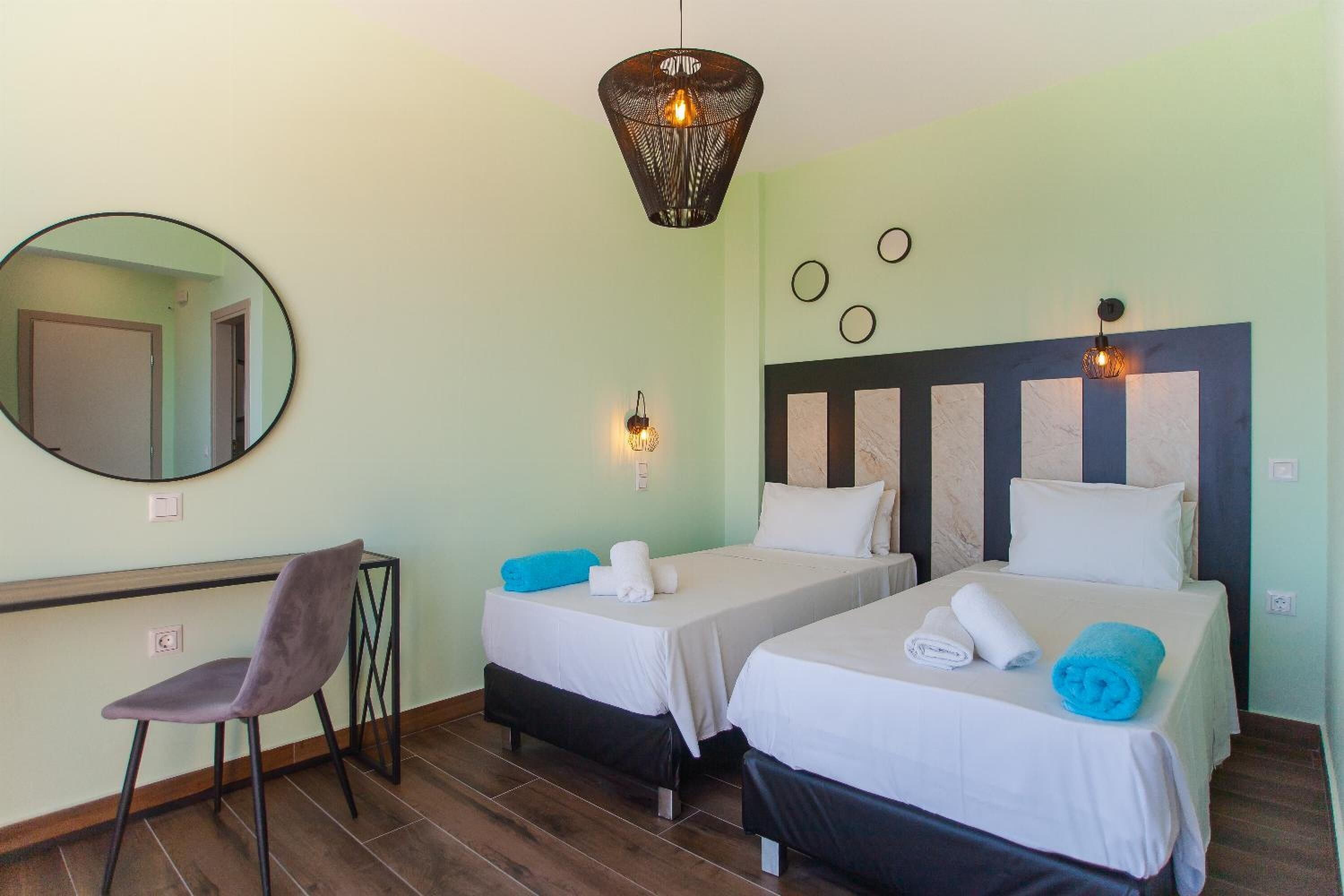 Een hotelkamer met twee bedden, een bureau, een stoel, een spiegel en een hanglamp.