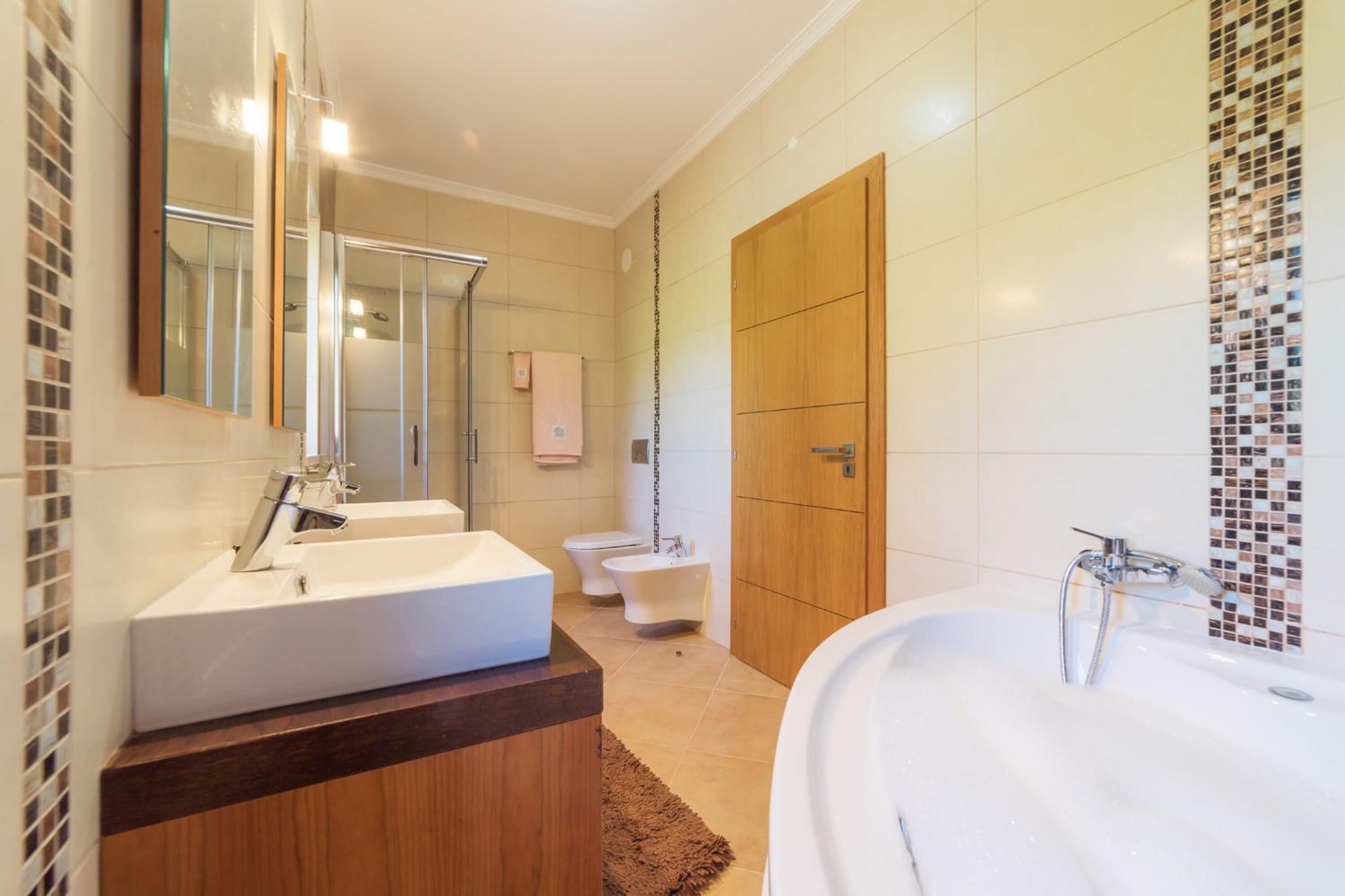 Een moderne badkamer met een groot bad, twee wasbakken, een douche en een toilet.