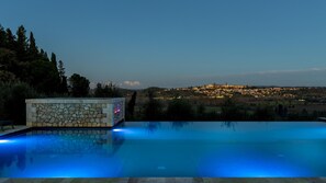 Una piscina con paredes de piedra y vista a un pueblo al anochecer.