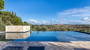 A swimming pool with a stone wall and a view of a town in the distance. - Villa Silvia 10 Emma Villas (Terricciola)