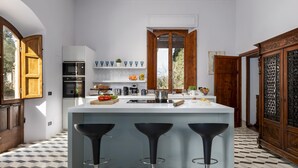 A modern kitchen with a central island, bar stools, and a view of the outdoors. - Villa Silvia 10 Emma Villas (Terricciola)