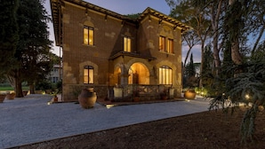 A two-story stone building with arched windows and a gravel driveway. - Villa Silvia 10 Emma Villas (Terricciola)