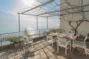 An outdoor dining area with a view of the sea, white chairs, a table set with plates and glasses, and a pergola structure. - Giuliano s House - Amazing Lake View (Laglio)