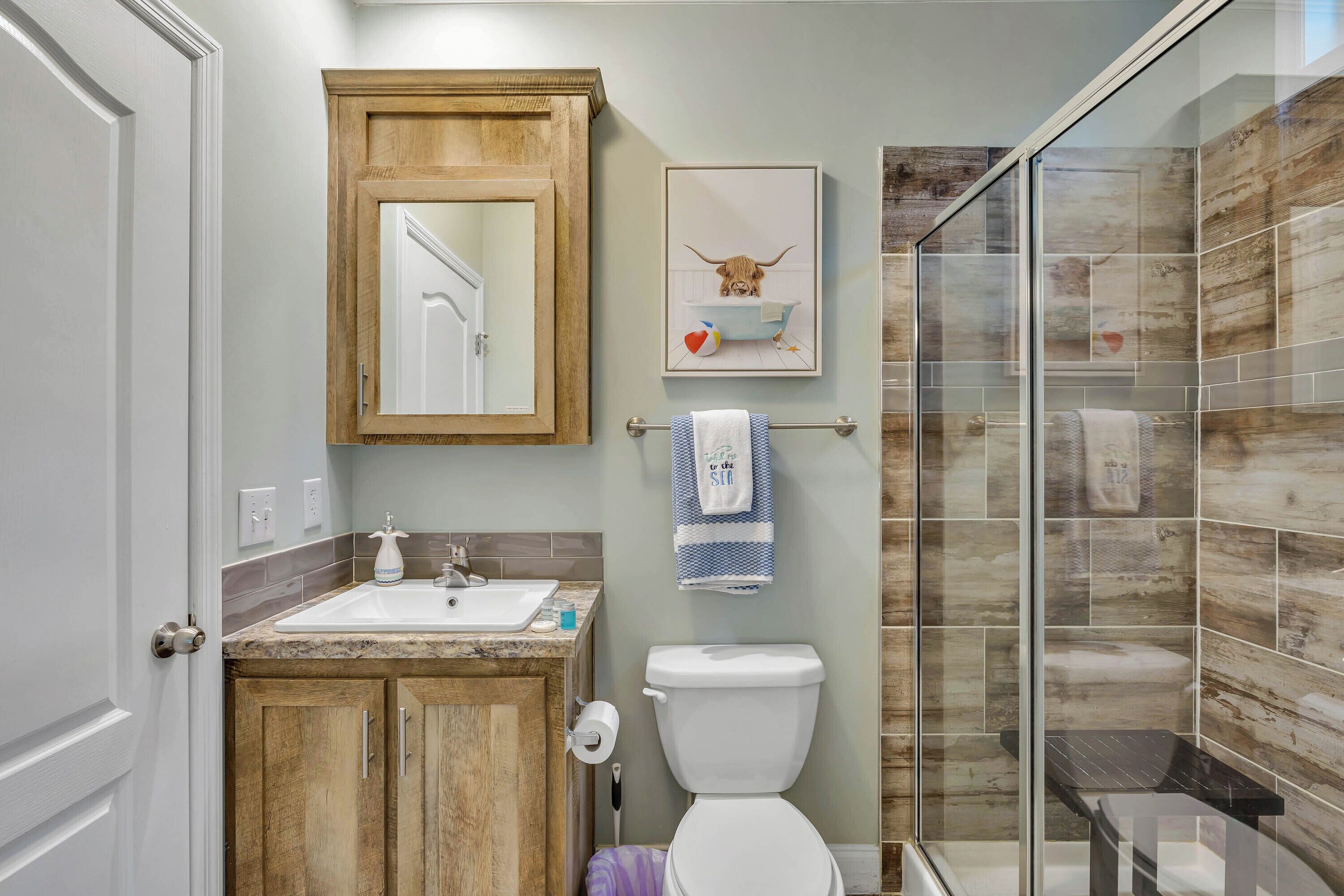 Un baño con tocador de madera, inodoro blanco, cabina de ducha de vidrio y una obra enmarcada en la pared.