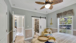 A bedroom with a bed, a ceiling fan, a window with a view, and a door leading to a bathroom.