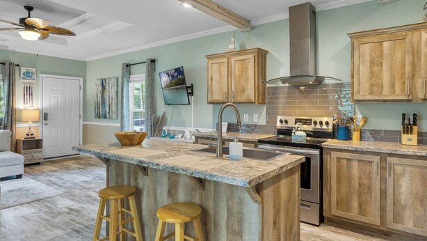 A spacious kitchen with wooden cabinets, a large island with stools, stainless steel appliances, and a ceiling fan.