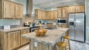 A kitchen with wooden cabinets, a stainless steel refrigerator, a granite countertop, and a wooden bowl centerpiece.