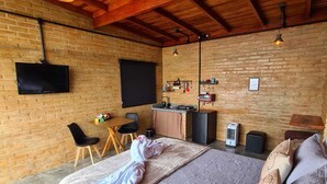A bedroom with a large bed, a desk, a TV, and a brick wall. - Chalé Sol no Horizonte  (Corrego do Bom Jesus)