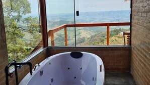 A hot tub in a room with large windows overlooking a scenic landscape. - Chalé Sol no Horizonte  (Corrego do Bom Jesus)