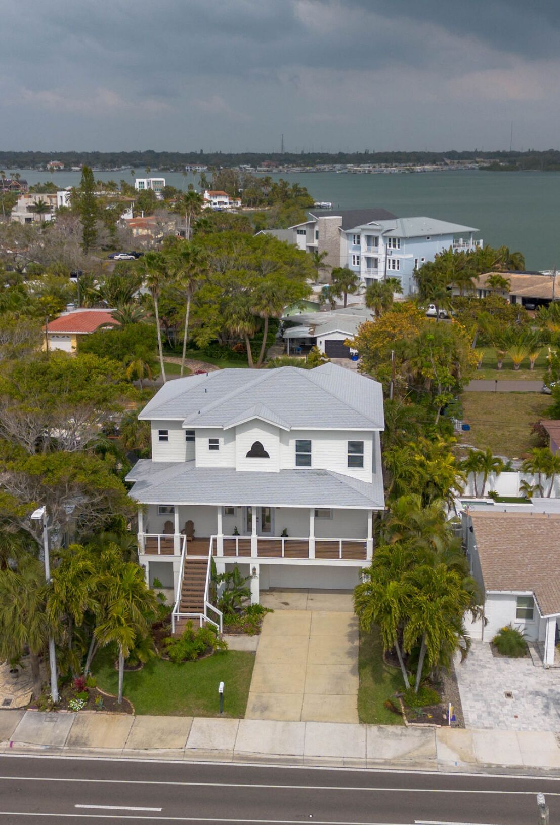 A two-story house with a front porch and a garage, surrounded by trees and a body of water in the background.