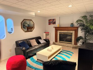 Una sala de estar con chimenea, un sofá, una mesita de centro y un reposapiés rojo.