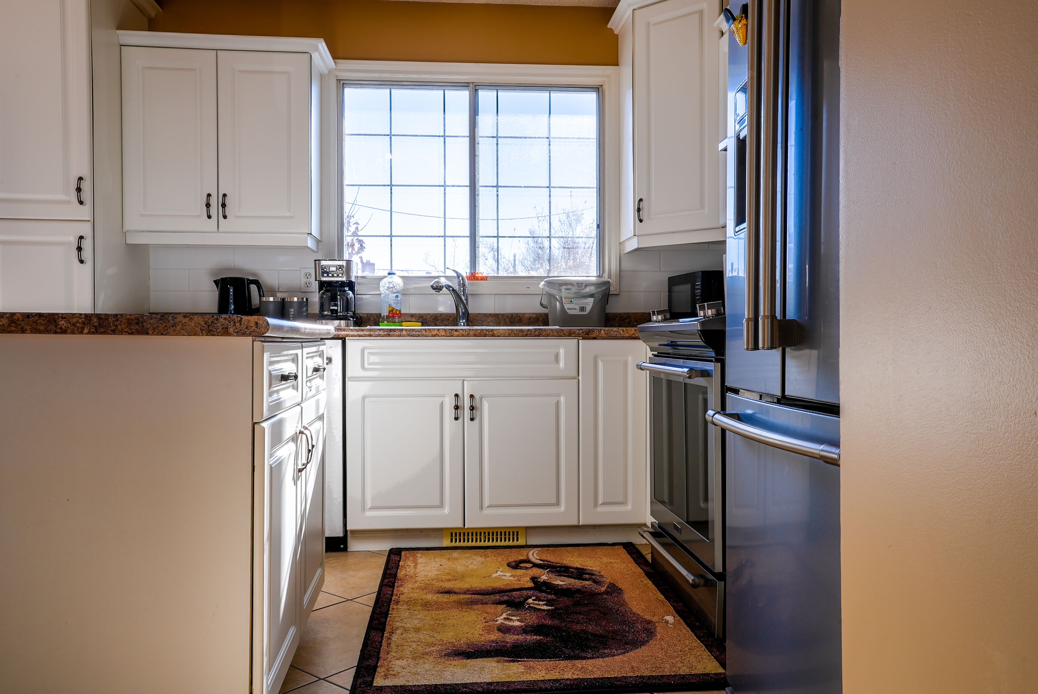 A kitchen with white cabinets, a stainless steel refrigerator, and a window above the sink.