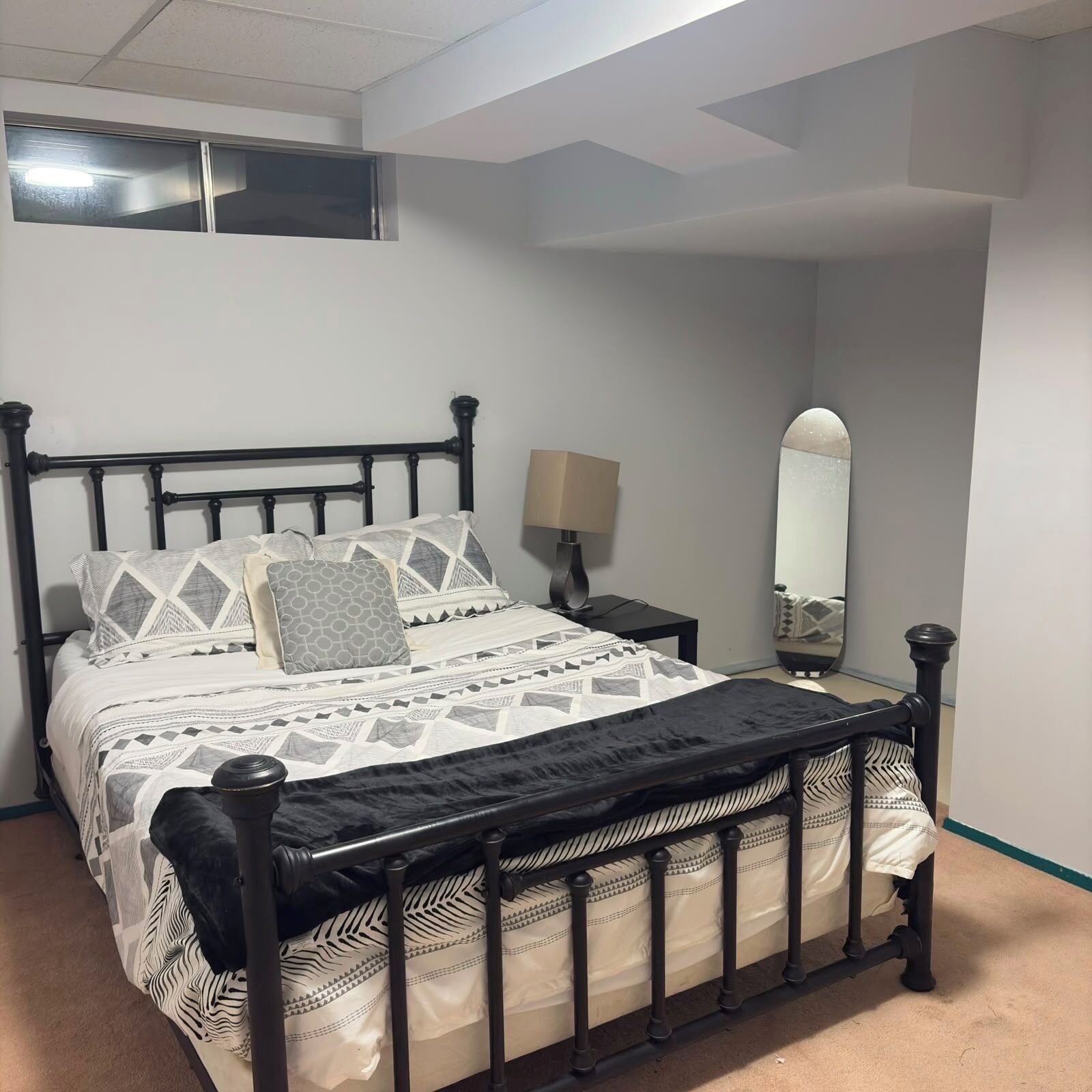 A bed with a black frame, a patterned bedspread, and pillows with geometric designs.