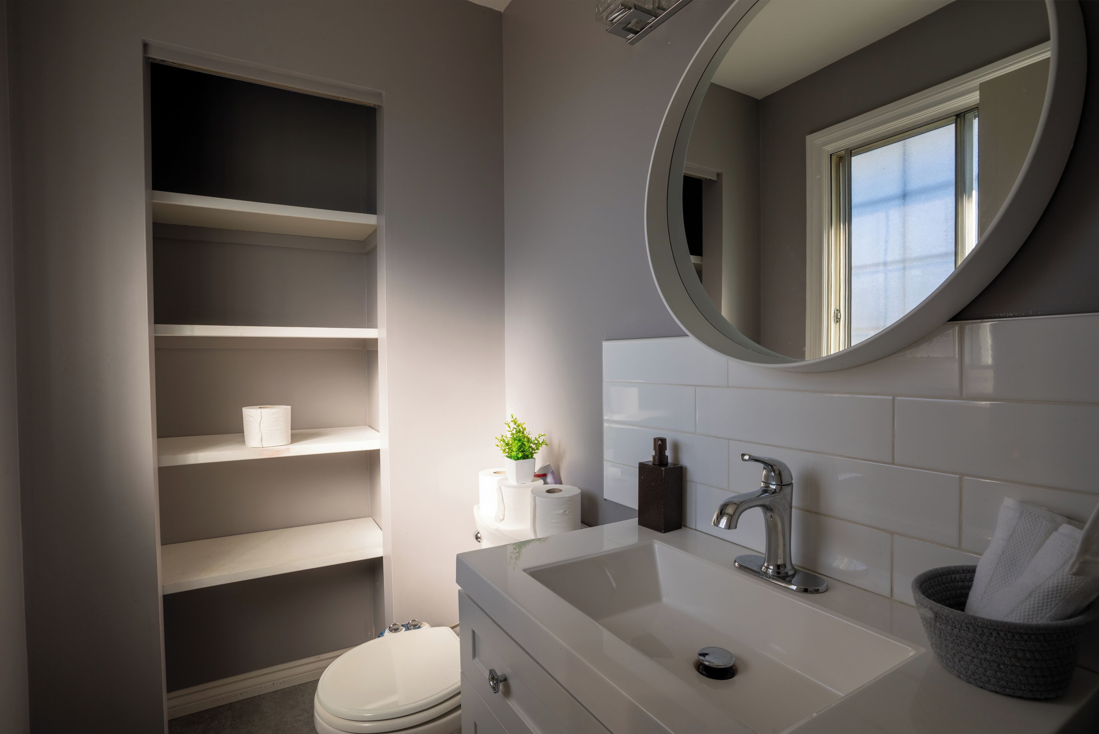A bathroom with a white sink, a mirror, a toilet, and built-in shelves.