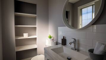 A bathroom with a white sink, a mirror, a toilet, and built-in shelves.