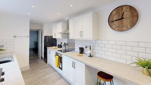 A modern kitchen with white cabinetry, a wooden clock, and a bar stool. - Central, Stunning 3-Bed House - Free Parking (Sunderland)