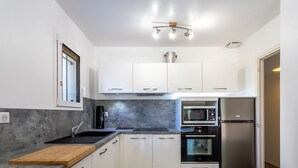 A modern kitchen with white cabinets, a granite countertop, a coffee maker, a microwave, an oven, and a stainless steel refrigerator.