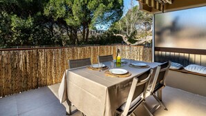 An outdoor dining area with a table set for two, a bamboo fence, and a view of trees.