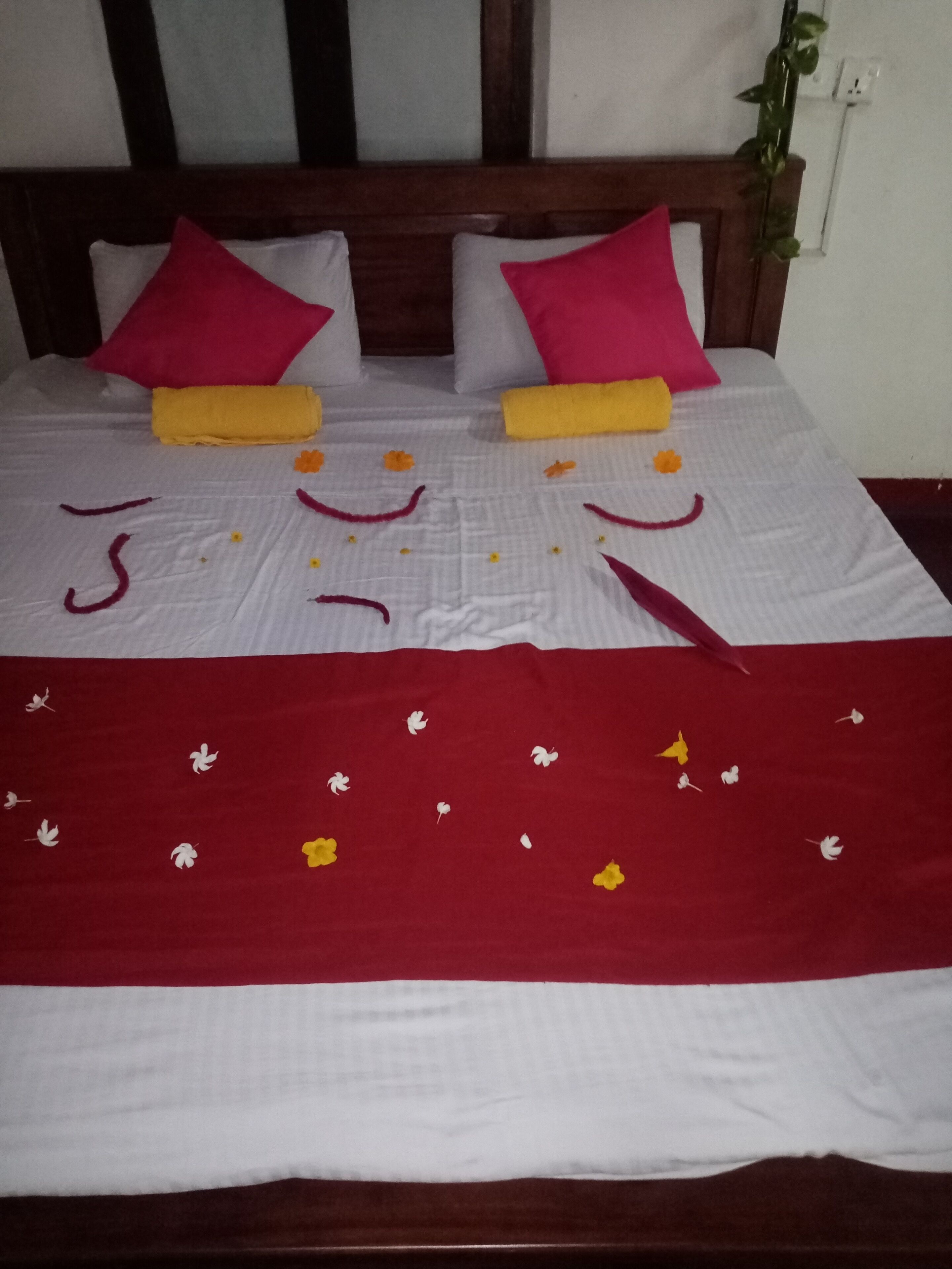 Un lit avec une couvre-lit blanche et rouge, deux oreillers rouges et des serviettes jaunes.